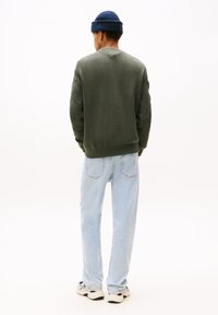 Olivengrønn genser med strukturert strikk, rund hals og ribbestrikkede mansjetter, parret med lyseblå jeans og casual sneakers. Bakview.