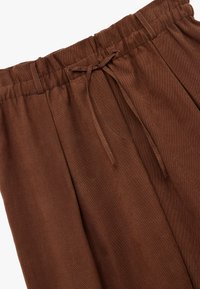 Bruine geplooide broek met een elastische tailleband en een koord. Glad textuur met een lichte glans en nette stikdetails.