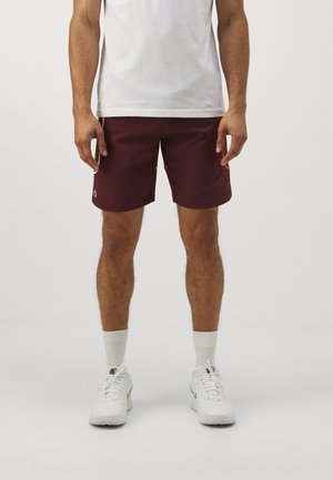 Bordeauxrode korte broek met een relaxte pasvorm, trekkoord in de taille en zijzakken. Gecombineerd met een effen wit T-shirt en witte sneakers.