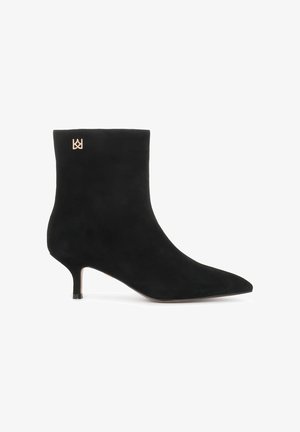 Fekete velúr bokacsizma hegyes orral és tüskés sarokkal. Arany logó részlet található a tetejénél. Simának és matt felületű.