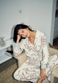 Set de pijamale crem cu model de caracatiță albastră și maro, format din cămașă și pantaloni. Țesătură moale și croială lejeră. Așezat pe un scaun deschis la culoare.