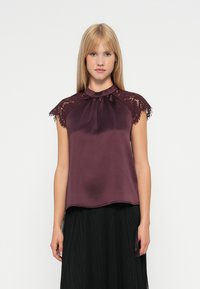 Top in satin color bordeaux con maniche in pizzo, caratterizzato da un collo arricciato e una vestibilità ampia, abbinato a una gonna nera plissettata.