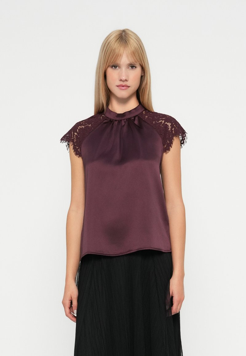 Top in satin color bordeaux con maniche in pizzo, caratterizzato da un collo arricciato e una vestibilità ampia, abbinato a una gonna nera plissettata.