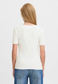 Weißes geripptes T-Shirt mit kurzen Ärmeln, rundem Halsausschnitt und gewellten Ärmelbündchen, kombiniert mit blauen hochgeschnittenen Jeans.