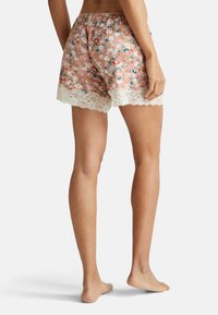Korte broek met bloemenpatroon op een lichtroze achtergrond, elastische tailleband en witte kantafwerking langs de zoom. Zacht stof, relaxte pasvorm.