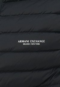 Schwarze Steppweste mit horizontalen Steppnähten und weißem "ARMANI EXCHANGE MILANO / NEW YORK"-Logo auf der Vorderseite.