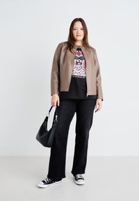 Chaqueta de cuero marrón, camiseta gráfica negra, pantalones anchos negros, bolso negro y zapatillas negras con suelas blancas. Fondo sencillo.