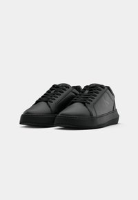 Zapatillas de cuero negro con puntas redondeadas, diseño con cordones, suela de goma texturizada y sutil branding en el lateral. Acabado mate suave.