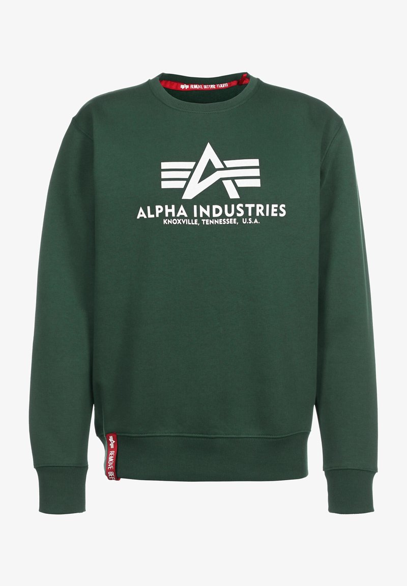 Sudadera verde oscura con cuello redondo, que presenta un logo impreso en blanco y el texto "ALPHA INDUSTRIES" en el frente. Etiqueta de acento roja en el dobladillo.