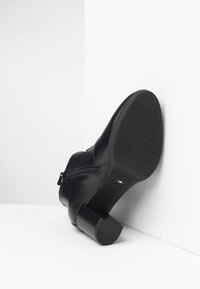Black leather ankle boot featuring a chunky heel, side zipper, and textured sole with a smooth finish and minimal detailing.