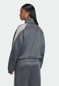 Γκρι αθλητική φόρμα με ψηλό γιακά, μακριά μανίκια και αντίθετα ανοιχτόγρια πάνελ ως διακοσμητικά στοιχεία. Ομαλή υφή με ελαστική μέση.