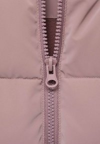 Pružená bunda z jemne ružového materiálu. Obsahuje centrálny zips so štruktúrovaným ťahačom a detailným prešívaním pozdĺž okrajov.