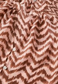 Tessuto rosa soffice con motivo a zigzag marrone, bottoni bianchi e pieghe arricciate vicino al bordo superiore.