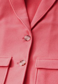 Blazer rosa corallo con rever eleganti, due tasche anteriori e bottoni trasparenti. Tessuto morbido e strutturato con dettagli di cucitura.