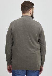 Suéter de punto gris con cuello alto, puños acanalados y parches en los codos. La parte trasera presenta una textura suave y un corte holgado. Combinado con jeans azules.