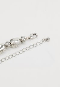 Bracelet en chaîne en argent avec des perles lisses et arrondies et un fermoir mousqueton. Les maillons de la chaîne sont en forme ovale avec une finition polie.