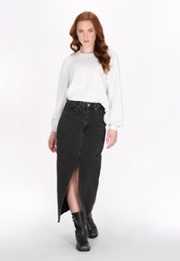 Maglia grigia a maniche lunghe abbinata a una gonna di jeans nera a vita alta con uno spacco frontale e stivali neri alla caviglia con fibbie.