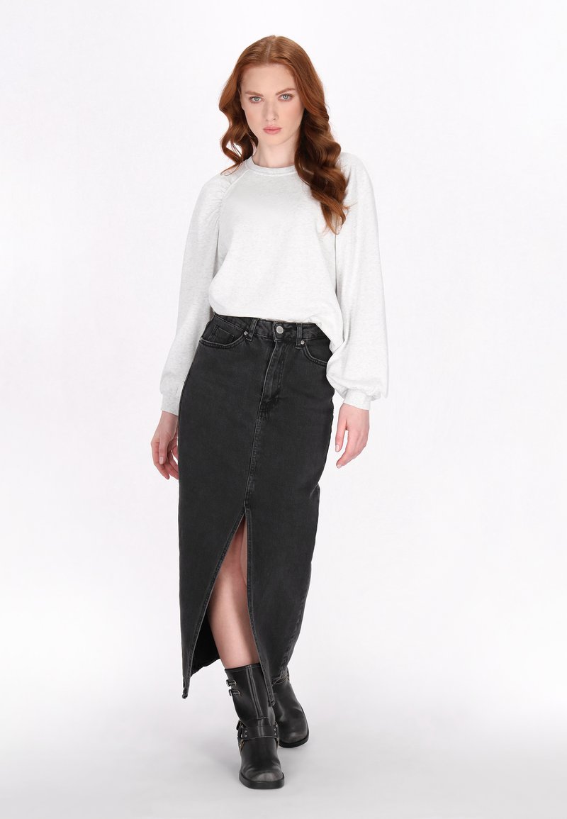 Maglia grigia a maniche lunghe abbinata a una gonna di jeans nera a vita alta con uno spacco frontale e stivali neri alla caviglia con fibbie.
