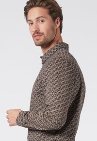 Camisa con estampado en marrón y crema, con diseños geométricos. Con cuello, mangas largas y una silueta ajustada. Textura suave.