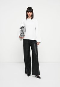 White long-sleeve shirt, black leather wide-leg pants, holding a textured black-and-white snake print clutch, and wearing black pointed heels.