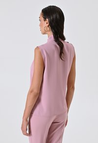Top senza maniche e a collo alto in tessuto rosa chiaro. Texture liscia con cuciture pulite. Abbinato a pantaloni aderenti coordinati per un look coerente.