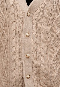 Beige knitted cardigan with cable and diamond patterns, featuring four round marbled buttons down the front.