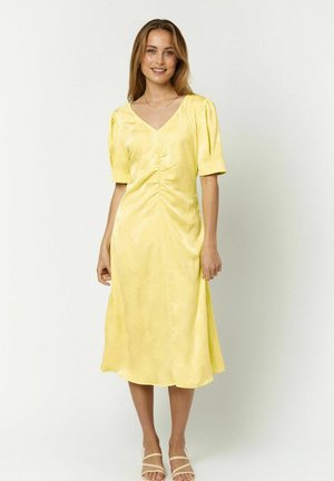 Vestido de satén amarillo con escote en V, mangas cortas abullonadas, detalles fruncidos en el busto y un dobladillo fluido de longitud media. Textura suave.