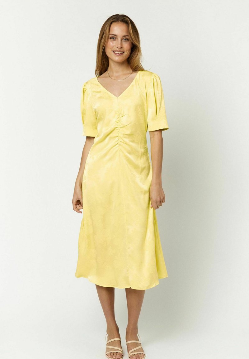 Gelbes Satin-Kleid mit V-Ausschnitt, kurzen Puffärmeln, gerafften Details an der Brust und einem fließenden, knielangen Saum. Glatte Textur.