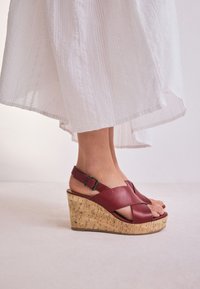 Rote Keilsandalen aus Leder mit Korkabsatz, ausgestattet mit gekreuzten Riemen und einem verstellbaren Einzelriemen. Strukturierter, offener Zehenbereich.