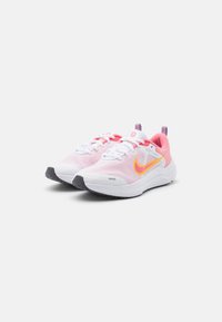 Scarpe sportive leggere in rosa e bianco, con una tomaia in rete senza cuciture, una suola ammortizzata e un logo giallo ben visibile di lato.