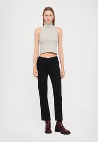 Top a collozzo grigio chiaro, a coste e accorciato; pantaloni neri attillati; stivali alla caviglia bordeaux lucidi con suola spessa; sfondo semplice.