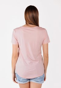 T-shirt en coton rose clair à manches courtes, col rond, ourlet incurvé, et coupe décontractée, accompagné de shorts en jean.