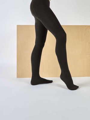Collants noirs côtelés en matériau lisse, ajustés, avec une taille haute et un design sans pieds, positionnés sur un fond en bois clair.