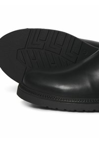 Botas de cuero negro con puntera redondeada y suela de goma texturizada. Presentan detalles cosidos y una superficie lisa y brillante.