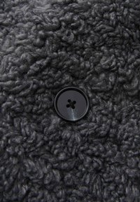 Black button on a textured dark gray fuzzy fabric, showcasing a looped, plush surface with fine detailing in the material's weave.