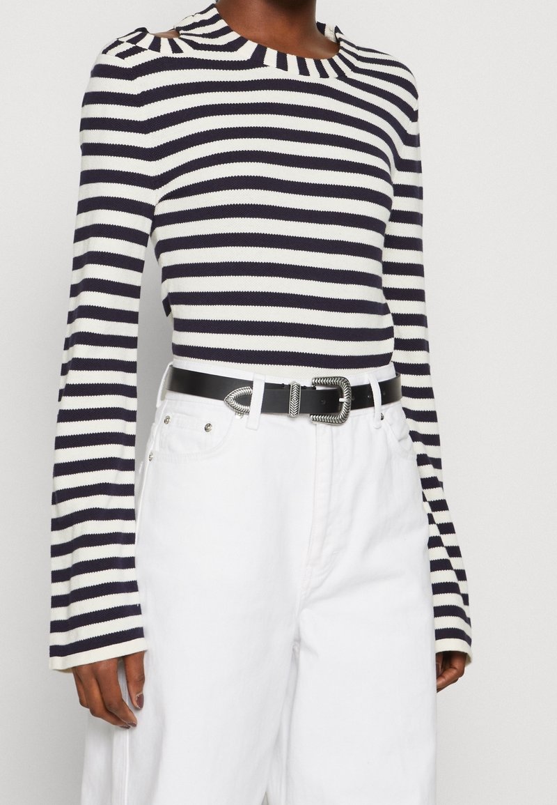 Navy und weiß gestreiftes Langarmoberteil mit einem Bootsausschnitt, kombiniert mit hochgeschnittenen weißen Hosen und einem schwarzen Gürtel mit einer silbernen Schnalle.