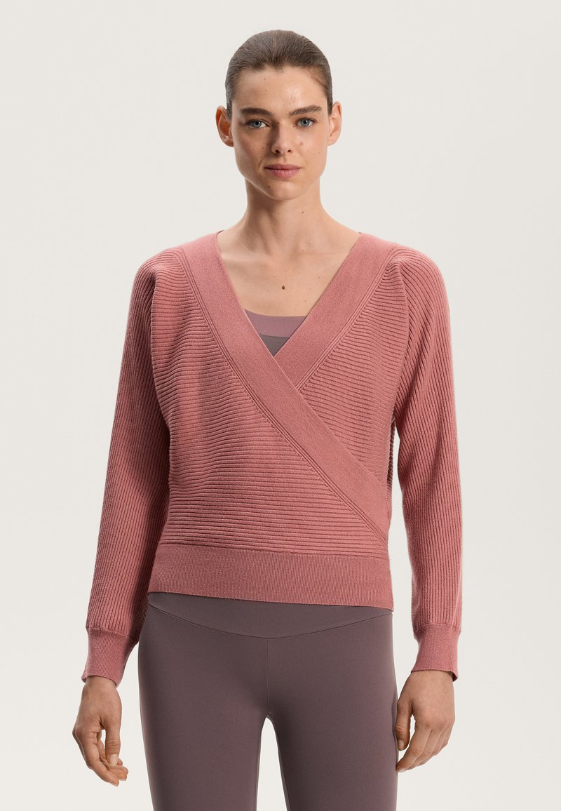 Pink wrap knit sweater with ribbed texture, deep V-neck, long sleeves, and fitted hem. Worn over a matching tank top and leggings.