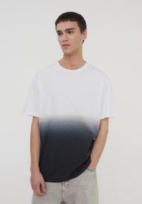 T-shirt bianco e blu navy con gradiente, maniche corte, scollatura rotonda, realizzata in cotone morbido, caratterizzata da una texture liscia e una vestibilità casual.