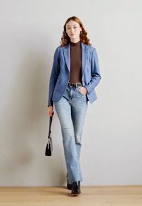 Světle modrý blazer přes hnědý rolák, spárovaný se světlými širokými džínami. Černé kotníkové boty a malá kabelka. Hladké materiály a volný střih.