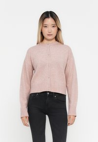 Ljust rosa stickad cardigan med rund halsringning, ribbad fåll och ärmslut, knappstängning och en avslappnad passform. I kombination med svarta jeans.