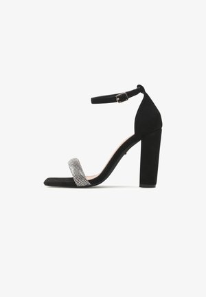 Sandalo nero con tacco a blocco, cinturino alla caviglia con fibbia e cinturino frontale decorato con piccoli strass.