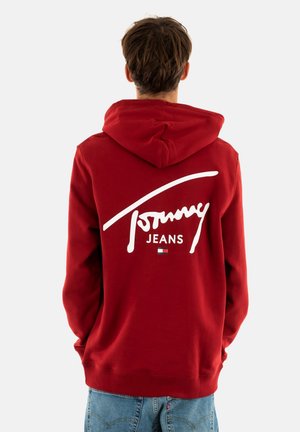 Sudadera roja con capucha ajustable, que presenta un gran logo blanco de "Tommy Jeans" en la parte posterior. Textura de tela suave, ajuste casual.