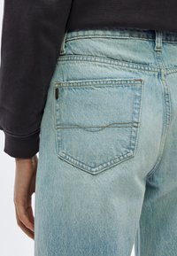 Svetlo modre jeans hlače z visokim pasom, ki imajo zadnji žep z nežnim šivom in teksturirano površino.