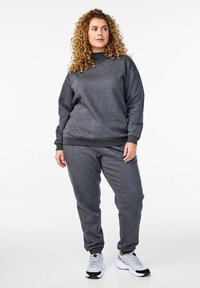 Felpa grigia e pantaloni jogger in morbido tessuto con colletto a girocollo e polsini a coste, abbinati a scarpe da ginnastica bianche.