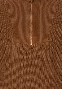 Bruine gebreide trui met een kwart-rits ontwerp, een gouden rits, gestructureerde ribbels en een rechthoekige gebreide patch op de borst.