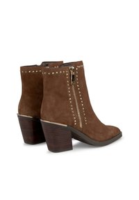 Stivaletti in suede marrone, alla caviglia, con punta affusolata, zip dorata e dettagli borchiati. Presentano un design con tacco grosso in legno.