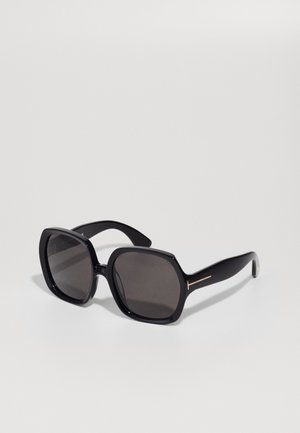 Lunettes de soleil noires surdimensionnées avec des verres foncés, de forme carrée et en plastique brillant. Présentent un subtil accent doré sur les branches.
