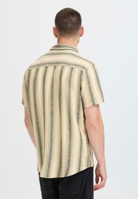 Korte mouwen overhemd in lichtbeige met verticale groene en grijze strepen, geweven textuur en een zachte kraag. Achteraanzicht toont een gebogen zoom.