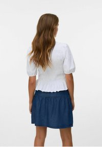 Haut blanc à manches bouffantes avec des détails smockés au dos, associé à une jupe en denim foncé à ourlet évasé.