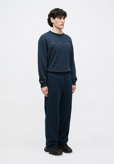 Granatowy dres z miękkiego materiału; składa się z bluzy z okrągłym dekoltem i akcentami z logo oraz luźnych spodni z elastycznym pasem.